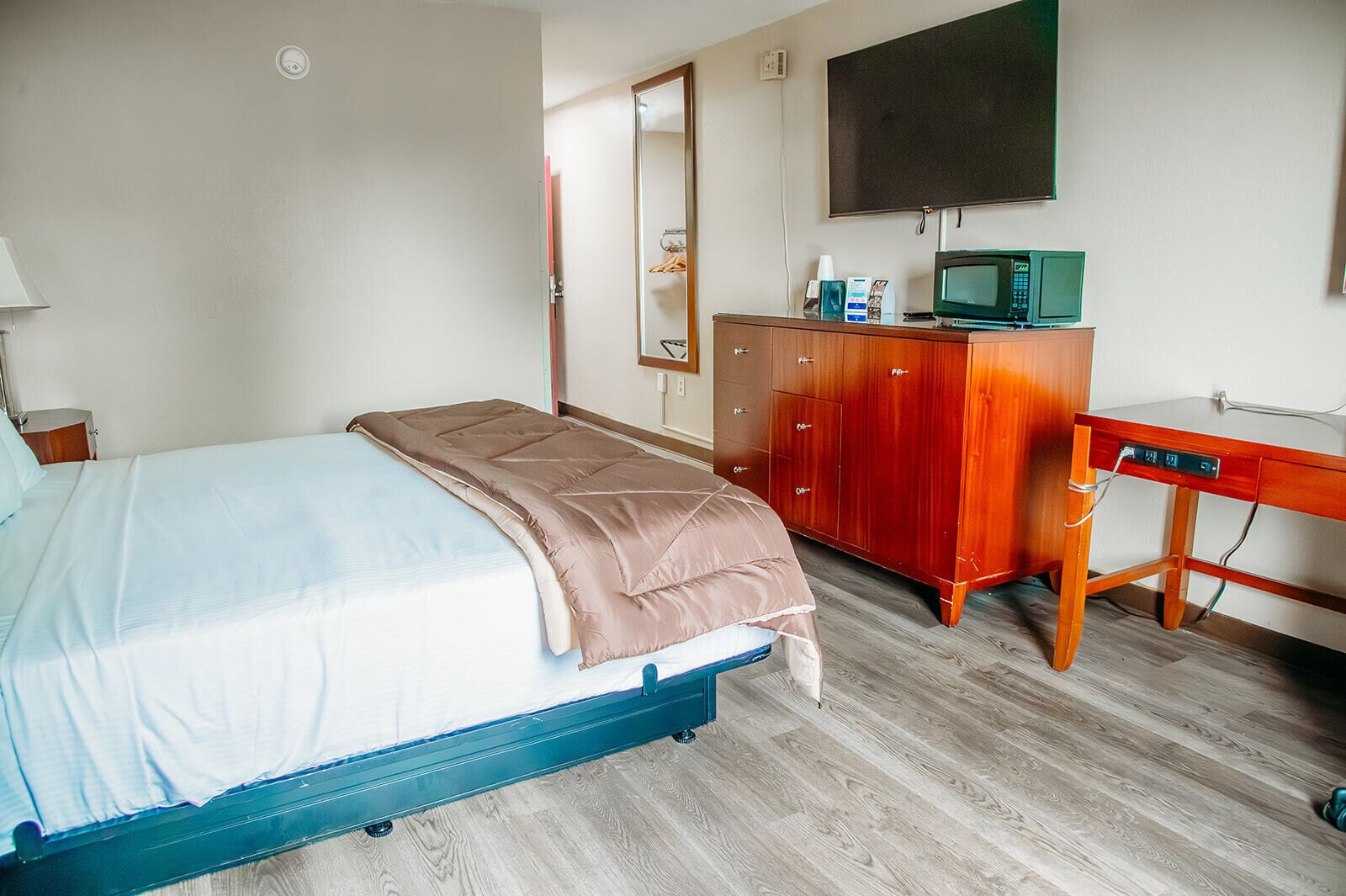 A hotel room with a bed, a wooden desk, a television, and a wardrobe.