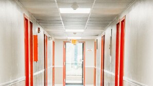 Un couloir d’hôtel avec un tapis à carreaux, des portes rouges et un panneau indiquant la sortie.