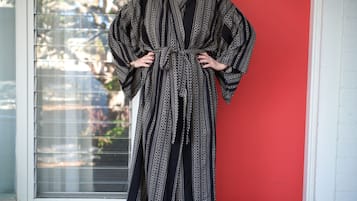 A person standing in front of a window with blinds, wearing a patterned robe.