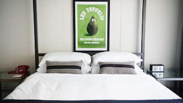 A neatly made bed with white linens and two patterned pillows, a red telephone, and a framed poster on the wall above the bed.