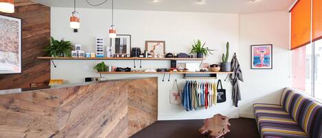 A modern reception area with a wooden reception desk, shelves with various items, a hanging coat rack, and a colorful sofa.