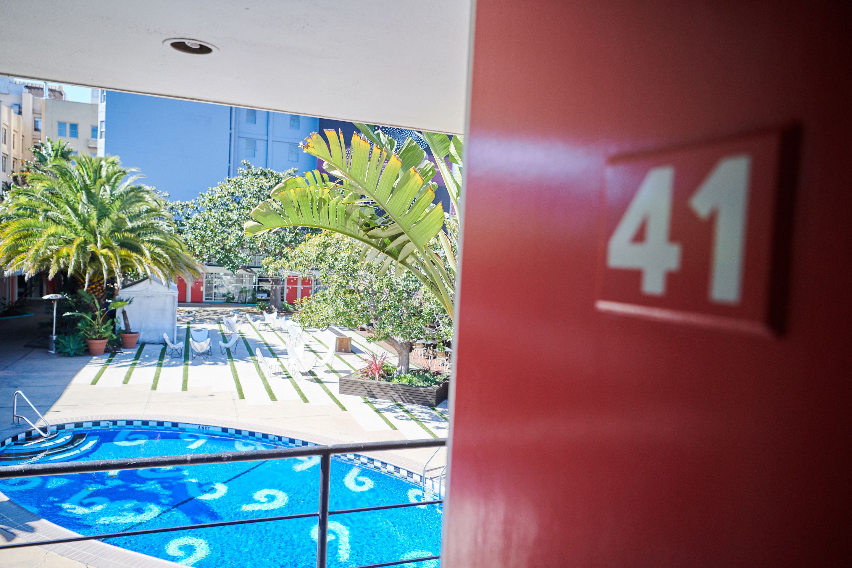 A pool area with a blue pool, palm trees, and a red wall with the number 41.