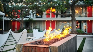 A fire feature in a planter, outdoor seating area, and a building with red accents in the background. - The Phoenix Hotel (San Francisco)