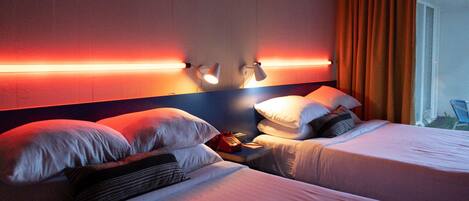 Habitación de hotel con dos camas, una mesita de noche con teléfono y lámparas de lectura fijadas a la pared.