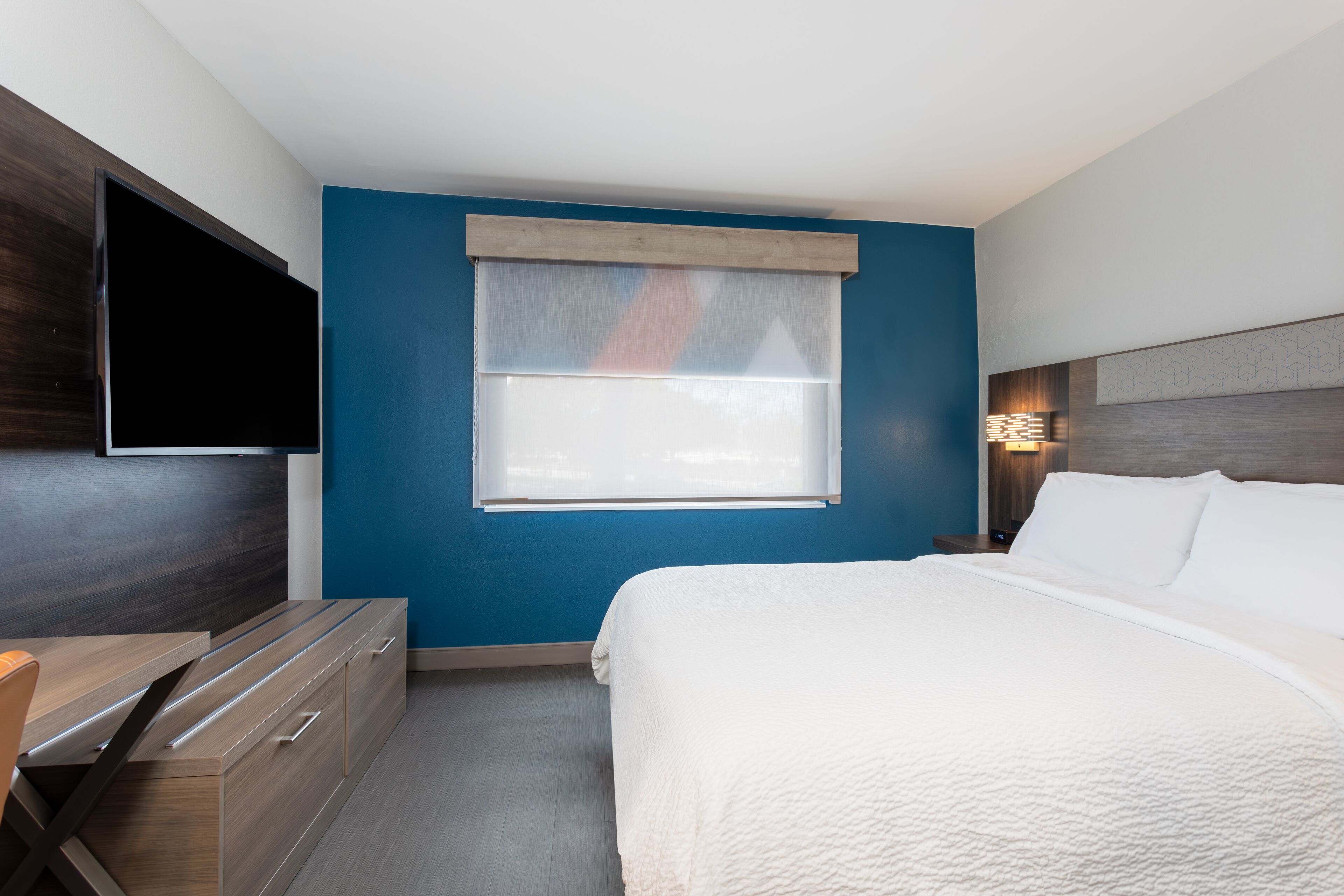 Una habitación de hotel moderna con una cama, un televisor montado en la pared, una ventana con vistas y un aparador de madera.