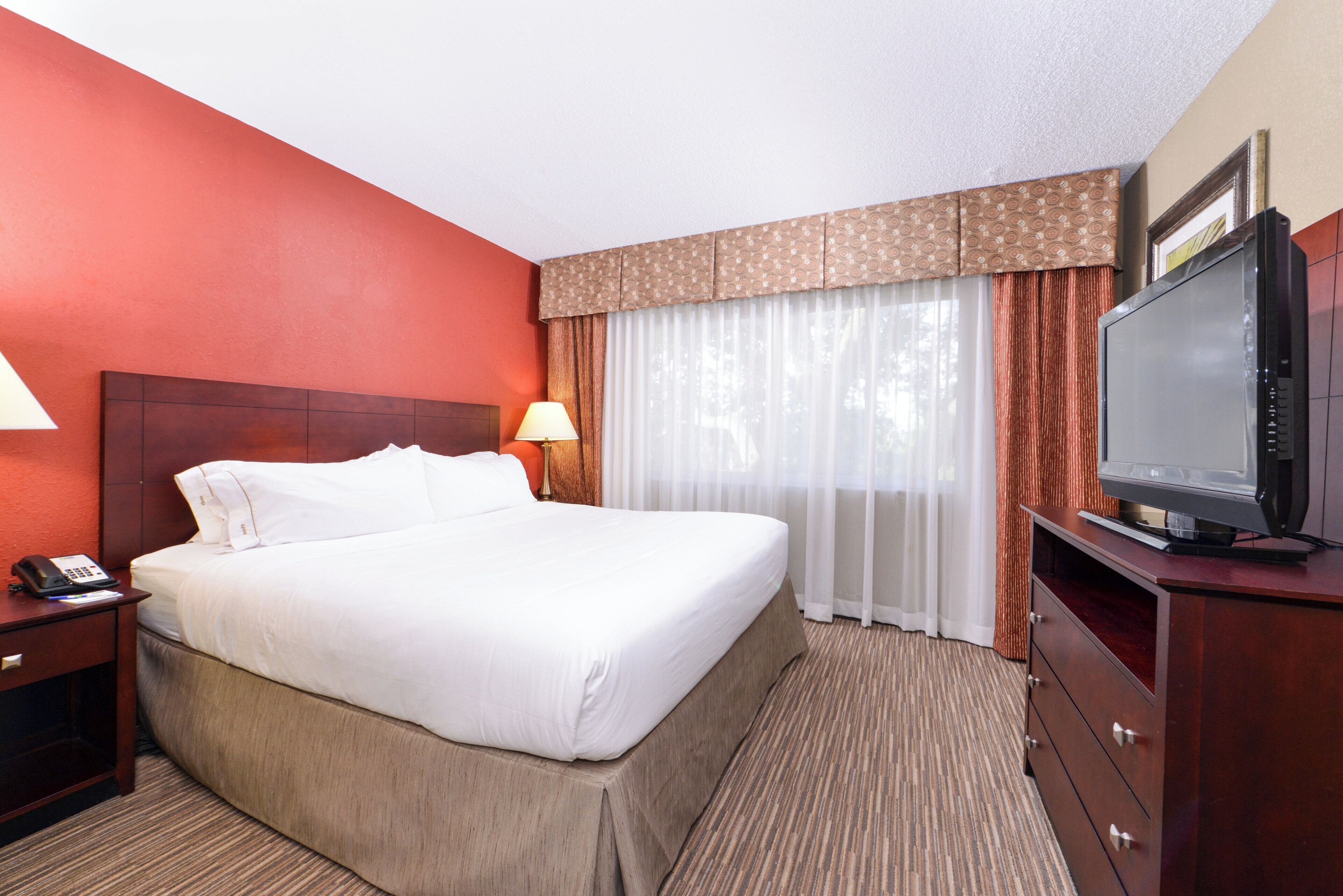 Una habitación de hotel con una cama grande, un televisor, una lámpara de noche y un teléfono.