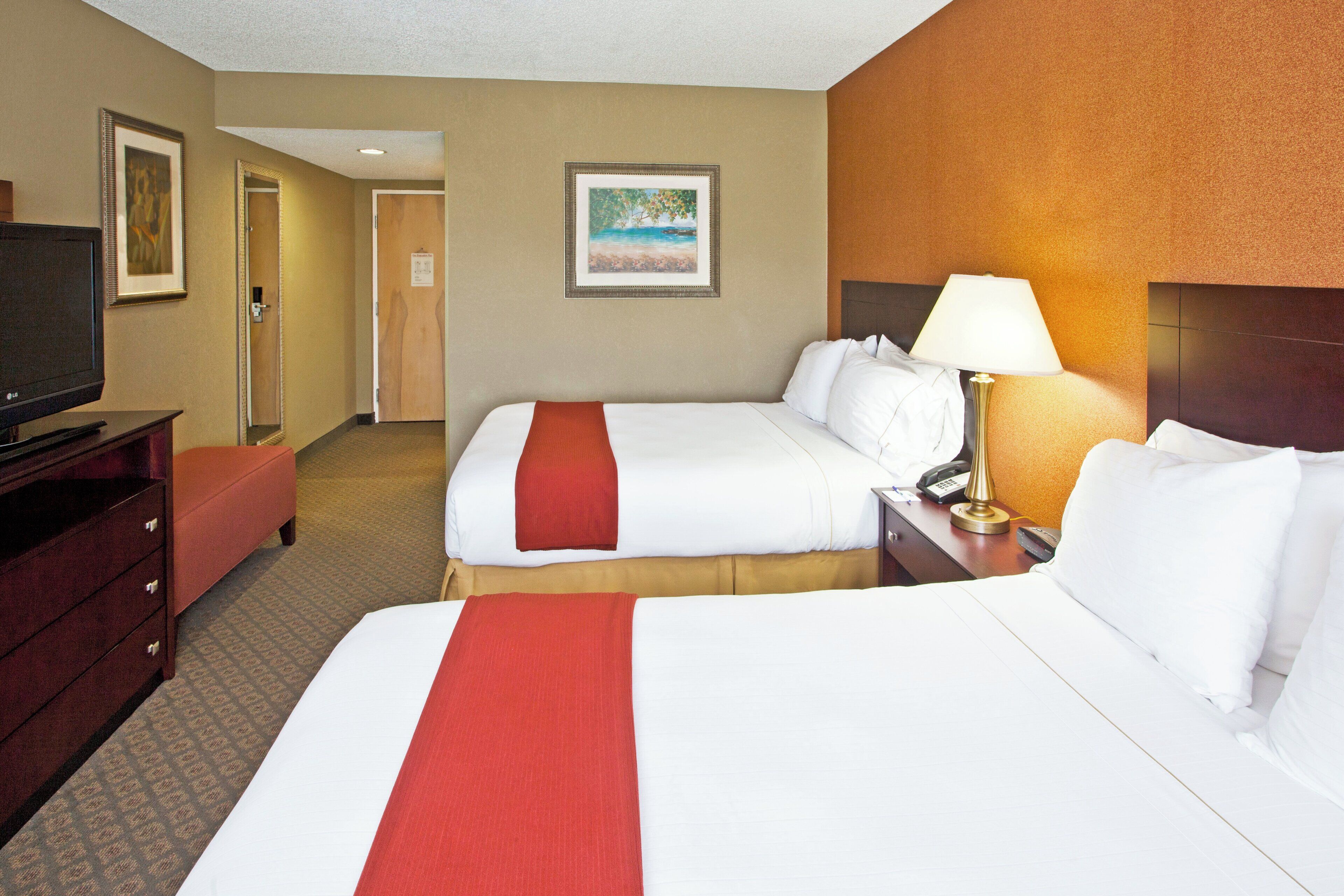 A hotel room with two beds, a TV, a desk, and a lamp.
