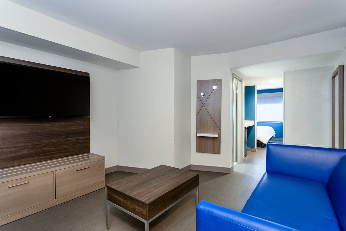 Een moderne hotelkamer met een flatscreen televisie, een houten bureau, een blauwe bank en een bed met een blauwe hoofdeinde.