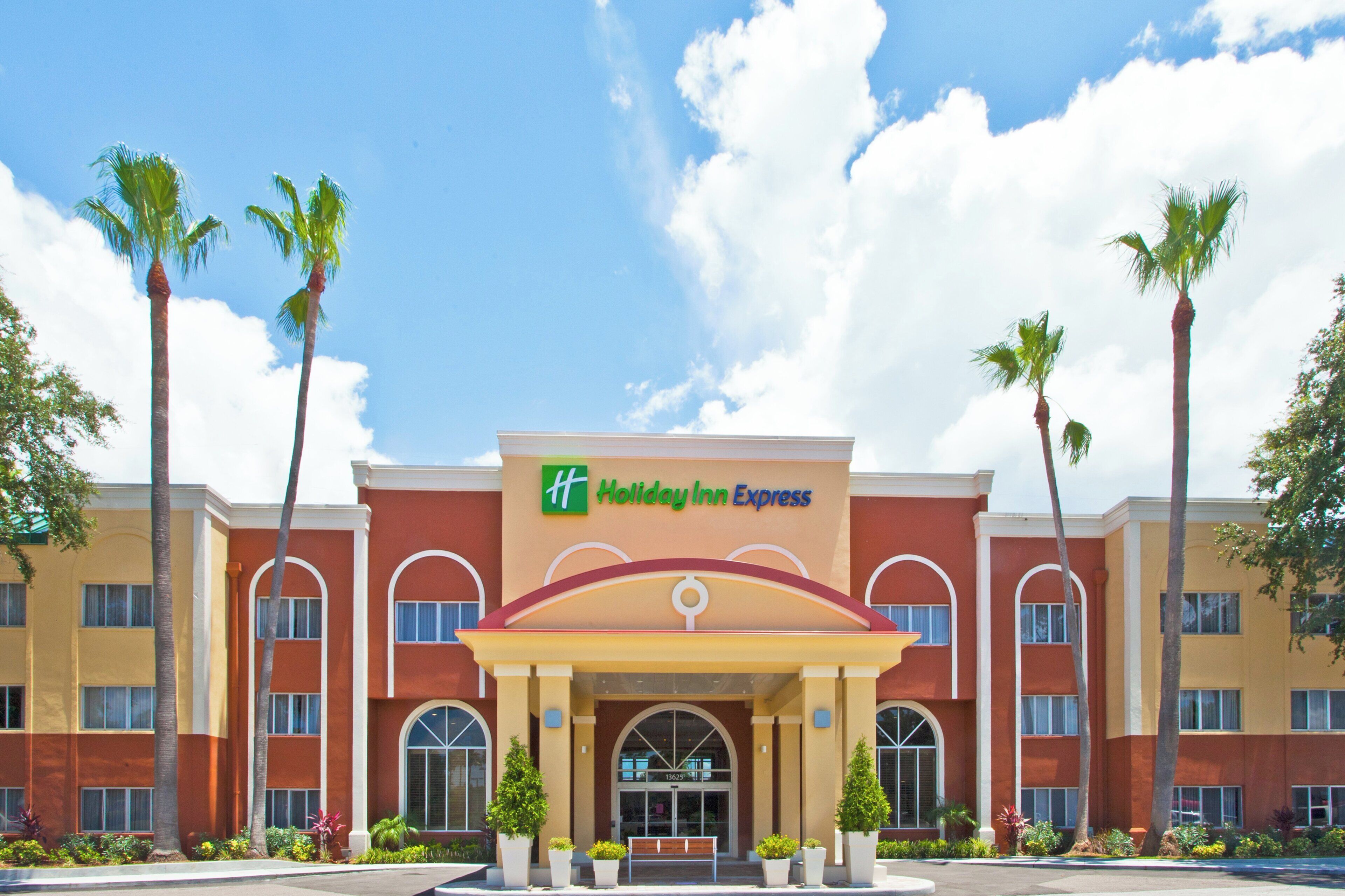 Ein Holiday Inn Express Hotel mit roter Fassade, Bogenfenstern und Palmen.