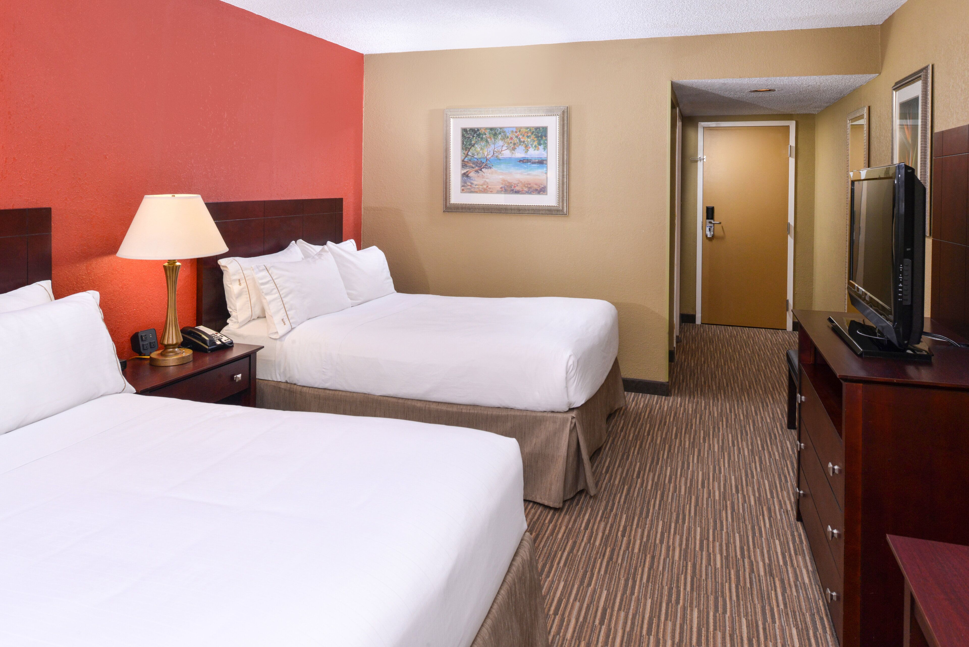 A hotel room with two beds, a TV, a lamp, and a painting on the wall.