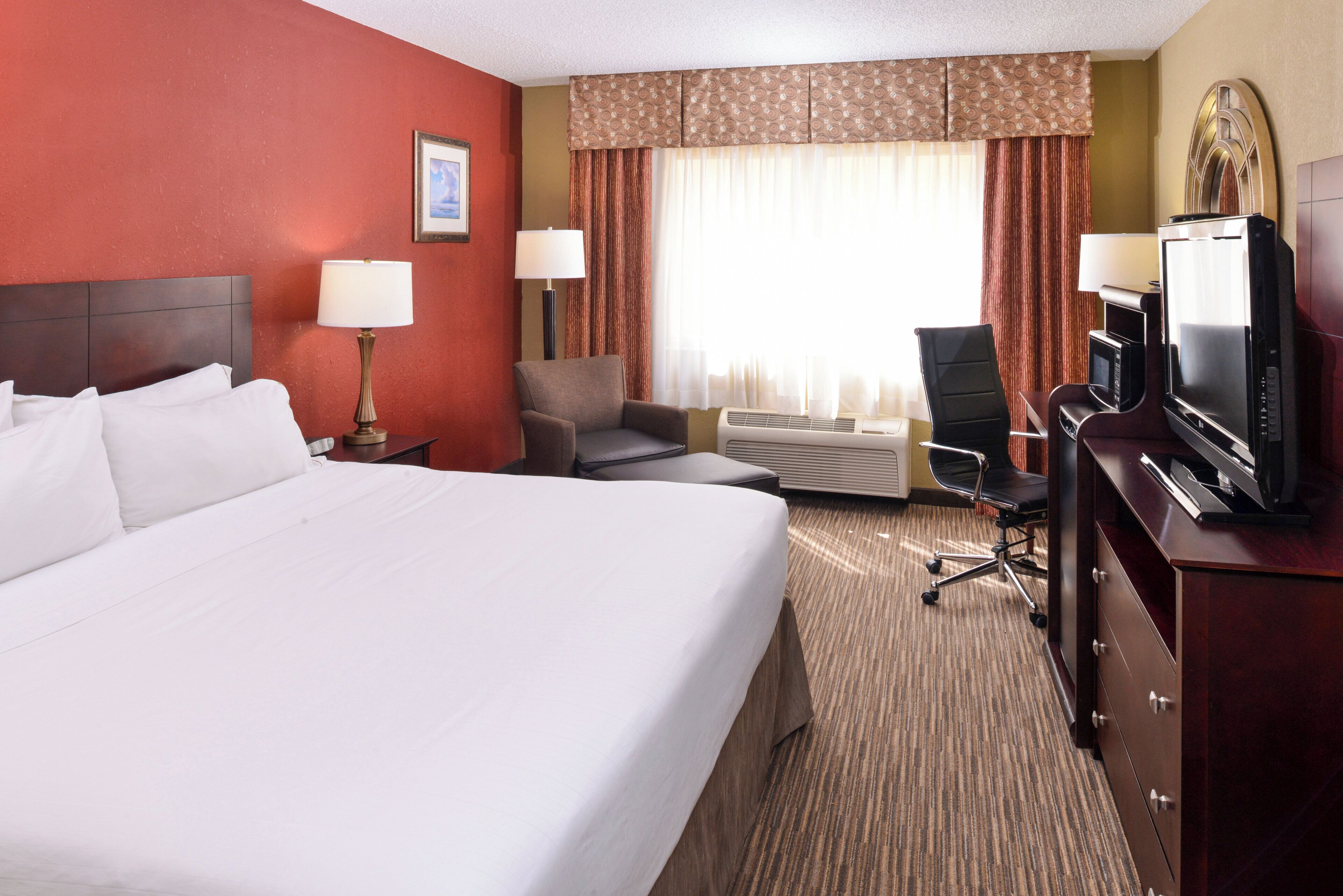 A hotel room with a large bed, two bedside lamps, a desk with a television, a chair, and a carpeted floor.