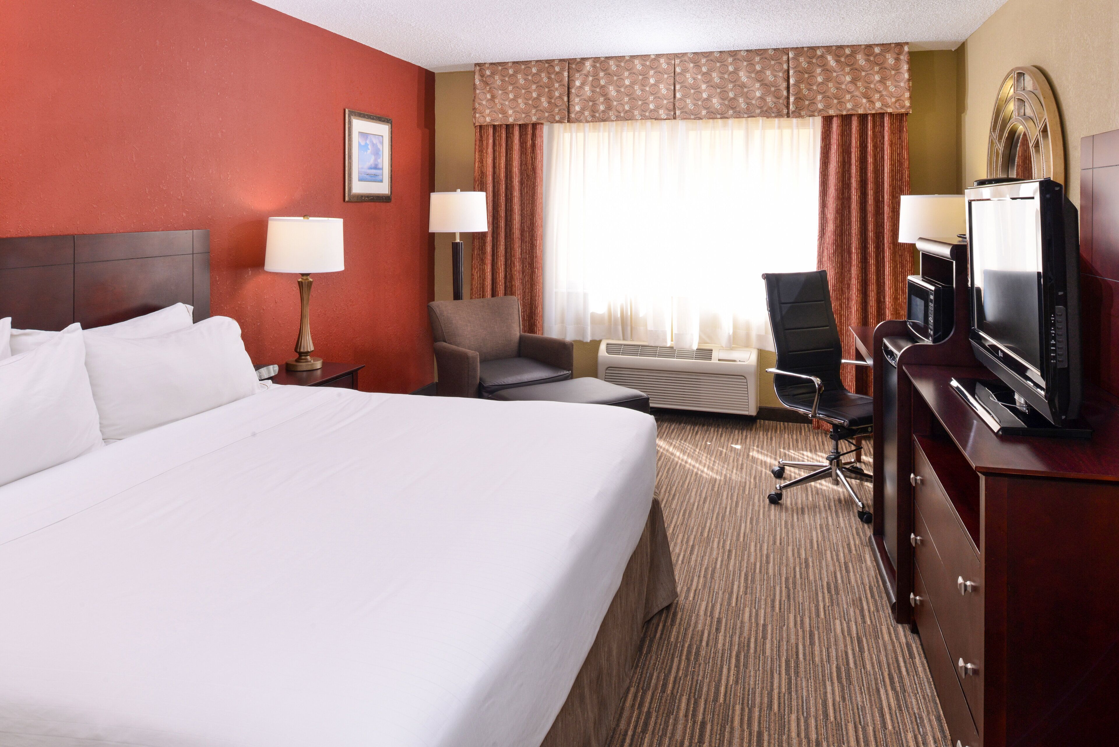A hotel room with a large bed, two bedside tables with lamps, a desk with a television, and a chair.