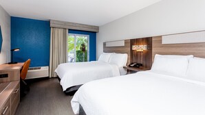Habitación de hotel con dos camas, un escritorio y una silla. Se aprecia una ventana con cortinas, un teléfono en la pared y una lámpara.