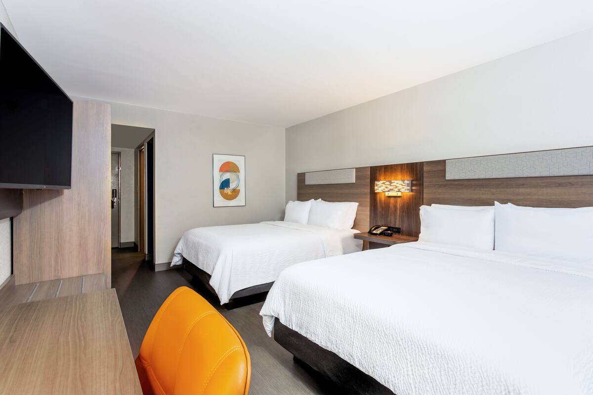 Een hotelkamer met twee bedden, een bureau, een televisie en een schilderij aan de muur.