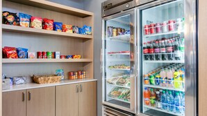 Una máquina expendedora llena de bocadillos y bebidas, y un refrigerador con distintos alimentos.