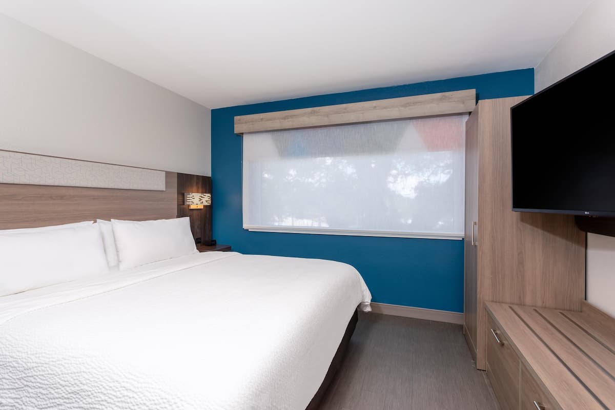 Ein Hotelzimmer mit einem großen Bett, einem Fernseher, einem Fenster mit Jalousien und einem Holzschrank.
