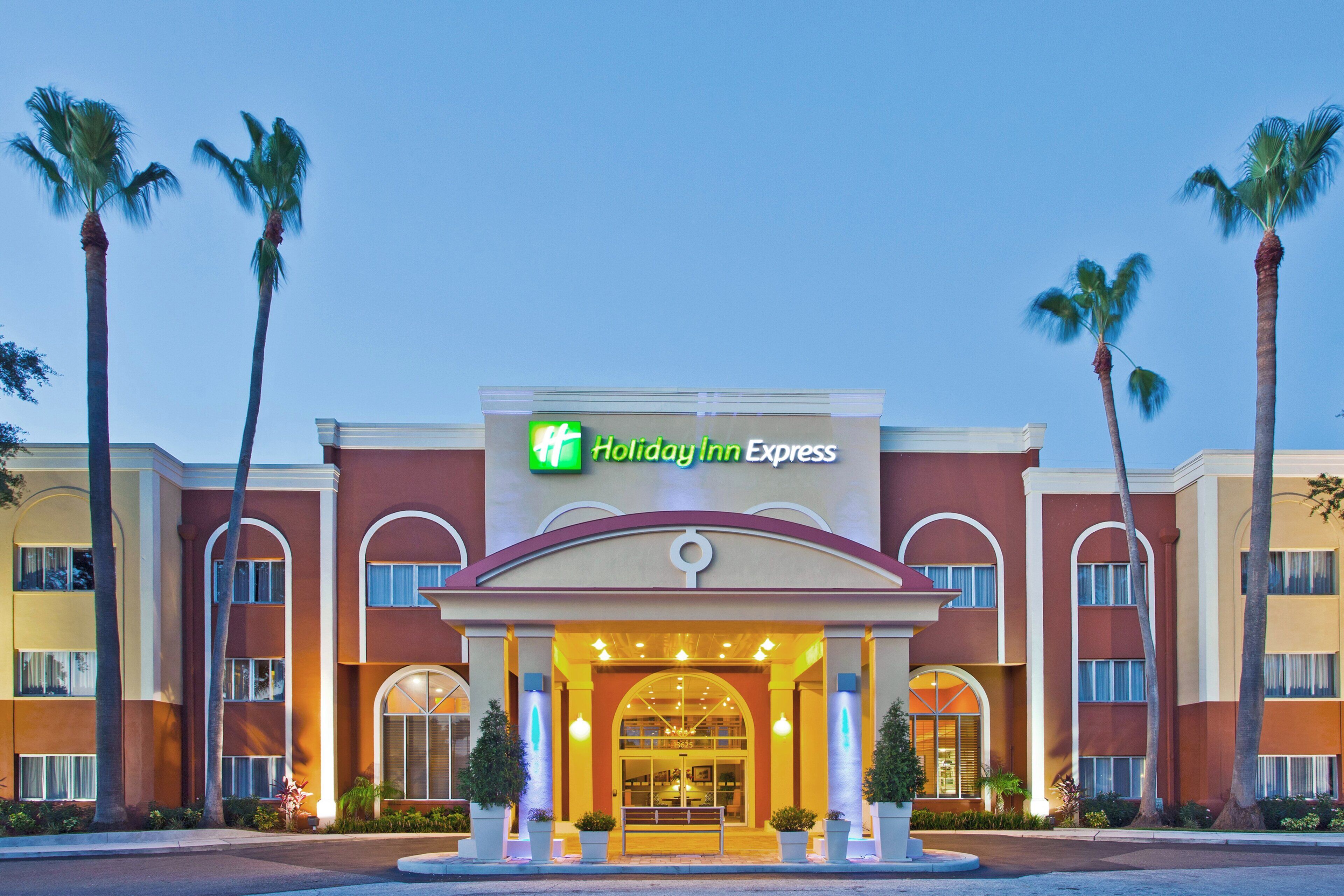 Um hotel Holiday Inn Express com entrada central, palmeiras e céu claro.