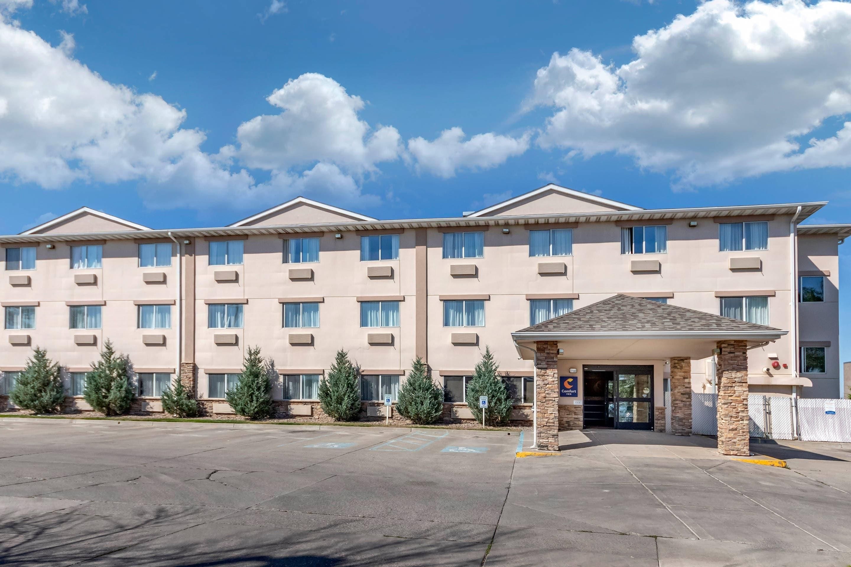 A multi-story hotel with a central entrance, a covered waiting area, and a parking lot.