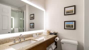A bathroom with a large mirror, two sinks, a toilet, and framed pictures on the wall.
