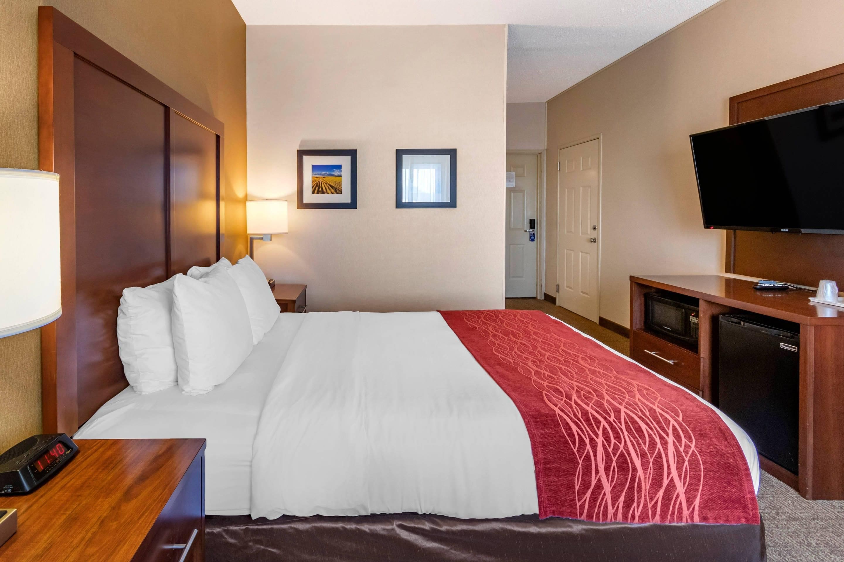 A hotel room with a large bed, a desk with a television, and a door leading to a bathroom.