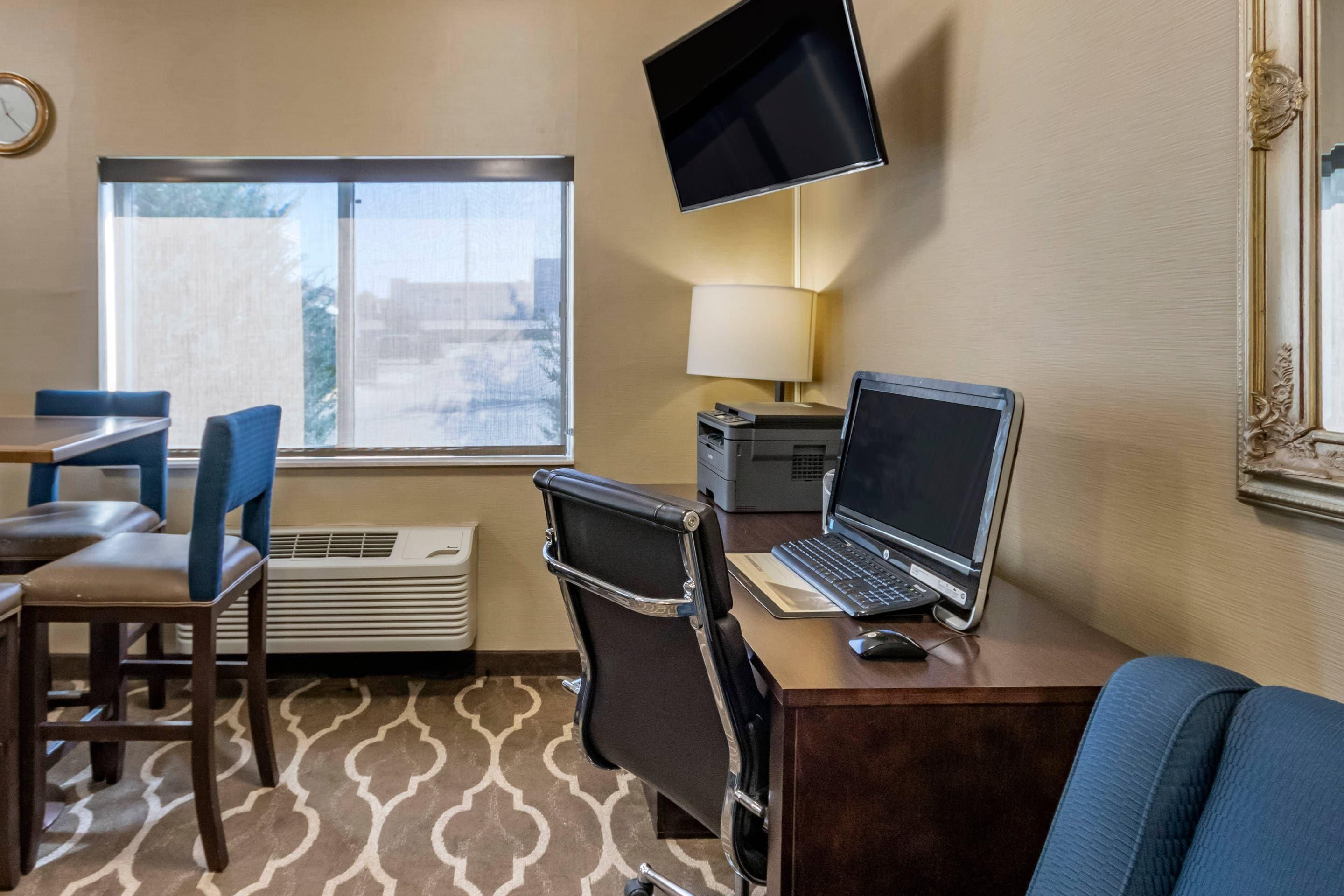 Ein Hotelzimmer mit Schreibtisch, Laptop und Fernseher. Ein Fenster bietet einen Ausblick, es gibt einen Sessel und eine Lampe.