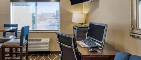 Hotelkamer met een bureau, laptop en televisie. Er is een raam met uitzicht, een stoel en een lamp.