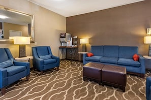 A hotel room with a blue sofa, two armchairs, a coffee machine, and a patterned carpet.