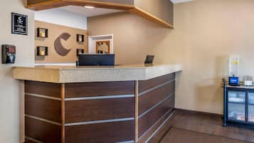 Un comptoir d’accueil avec un panneau décoratif en bois, un grand logo en forme de C sur le mur et un petit coin salon équipé d’une machine à café.