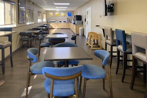 A cafeteria with multiple tables and chairs, a kitchen area, and a television mounted on the wall.