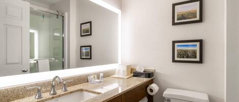 Un baño con un espejo grande, dos lavamanos, un inodoro y cuadros en la pared.