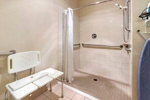 Eine barrierefreie Dusche mit Sitzbank, Haltegriffen und gefliestem Boden in Weiß.