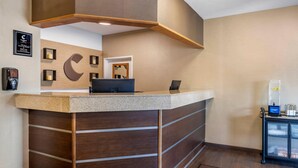 A reception desk with a wooden panel design, a large C-shaped logo on the wall, and a small seating area with a coffee machine. - Comfort Inn Great Falls South (Great Falls)