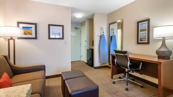 A hotel room with a sofa, a desk, a chair, a lamp, and a small table.
