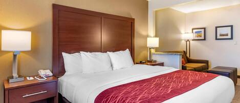 A hotel room with a large bed, two bedside tables, a nightstand, a desk, a chair, and two lamps.