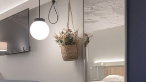 A modern hotel room with a blue sofa, a large mirror reflecting the bed, a hanging plant, and a small table with a book and headphones. - ibis Rueil-Malmaison Centre (Rueil-Malmaison)