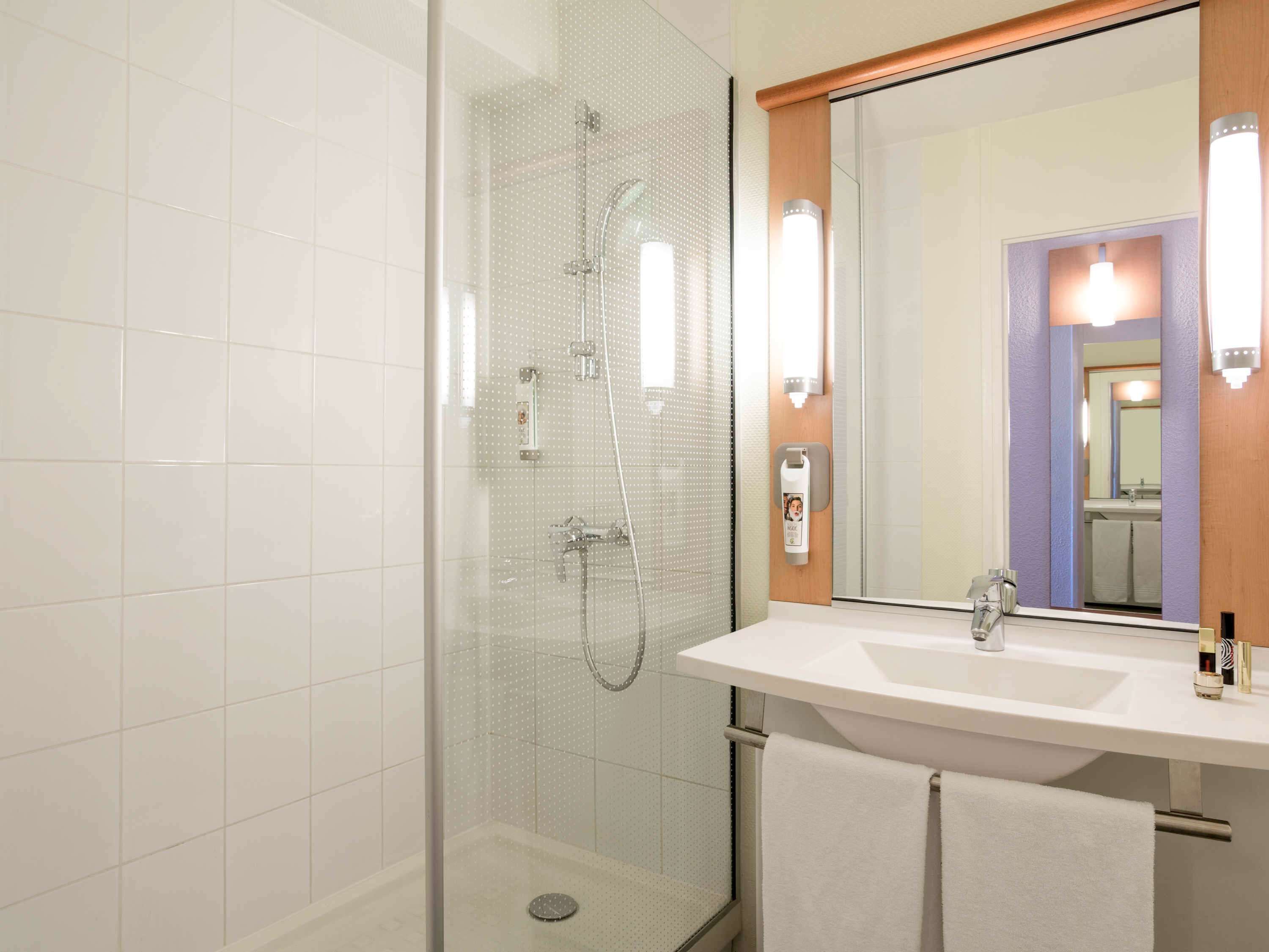 Une salle de bain moderne avec une douche à parois de verre, un lavabo blanc et un grand miroir.