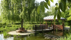 A wooden gazebo with a metal roof over a pond with lily pads, surrounded by lush greenery and a bench. - ibis Rueil-Malmaison Centre (Rueil-Malmaison)