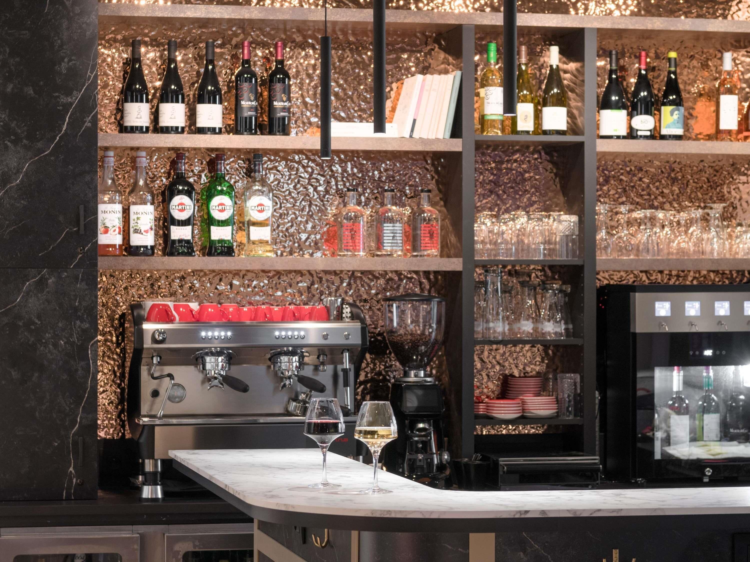 A bar area with shelves of wine bottles, a coffee machine, and glasses.