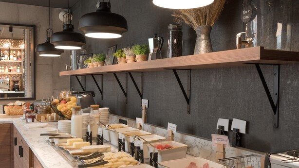 A buffet setup with various food items, a coffee machine, and hanging lights. - ibis Rueil-Malmaison Centre (Rueil-Malmaison)