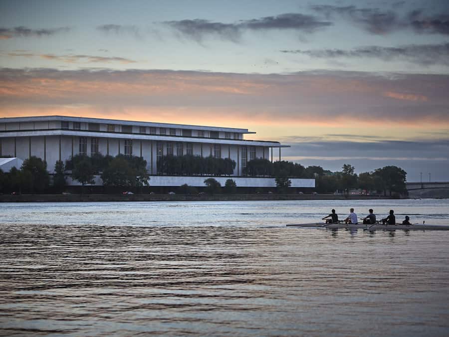A modern building with a flat roof and large windows, located beside a calm river.