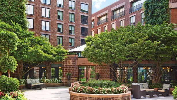 A courtyard with brick buildings, outdoor seating, and lush greenery. - Four Seasons Hotel Washington DC (Washington)