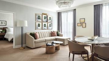 A modern hotel room with a beige sofa, a round dining table, and a chandelier.