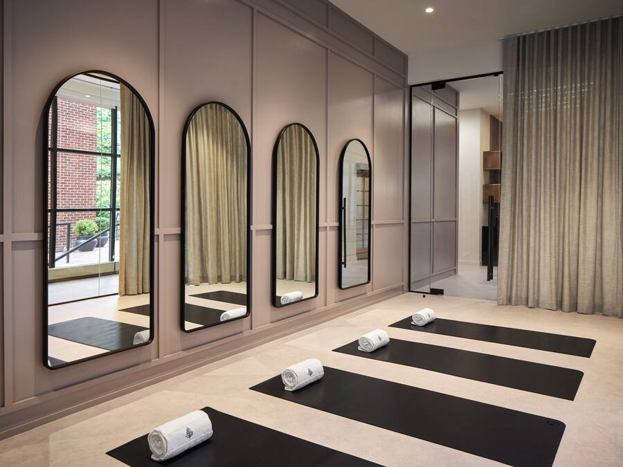 A modern hotel room with large mirrors, black and beige mats, and neatly rolled towels.