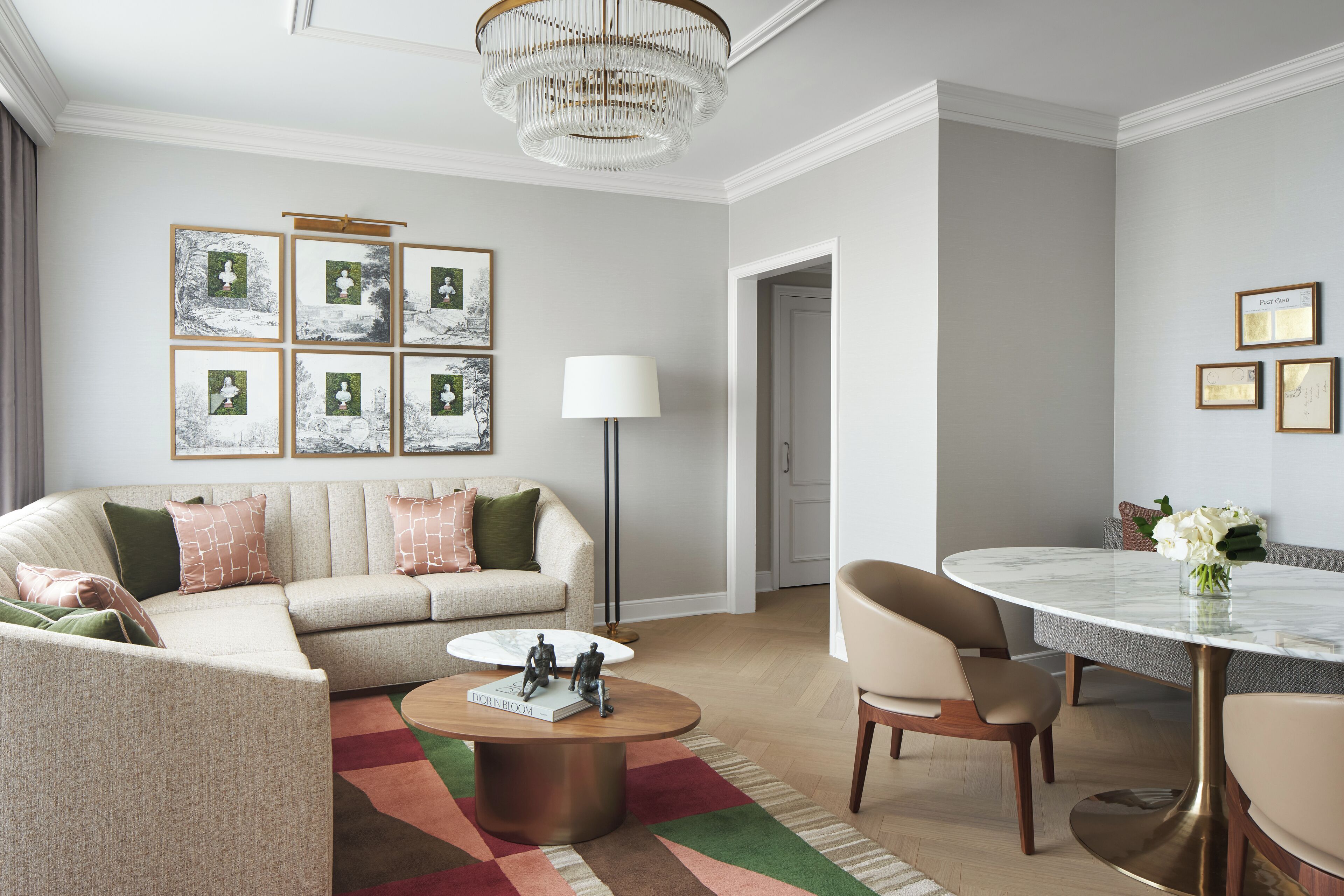 A modern living room with a beige sofa, a round coffee table, and a dining area with a marble table and chairs.