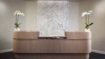 A reception desk with two vases of white orchids, a marble-like decorative piece, and a vertical striped wall in the background.