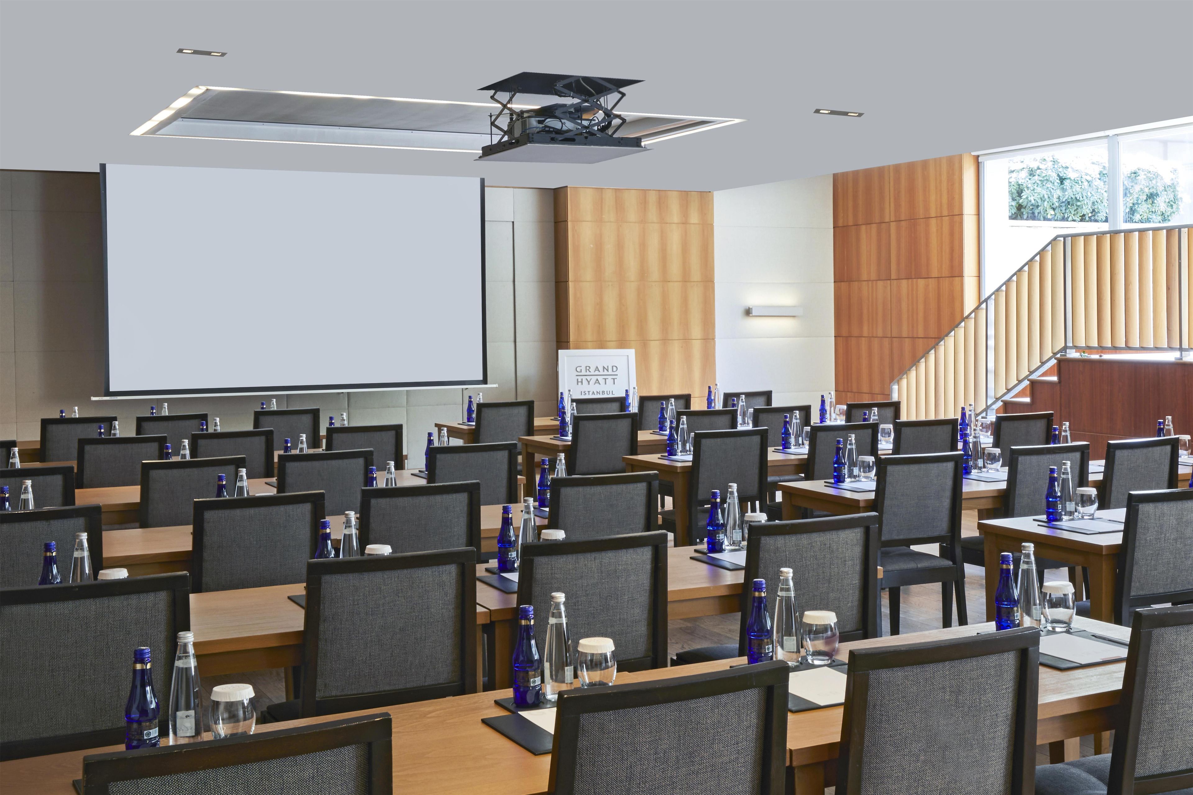 Ein Konferenzraum mit mehreren Tischen, Stühlen und einer großen Leinwand.