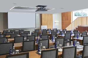 A conference room with multiple tables, chairs, and a large screen.