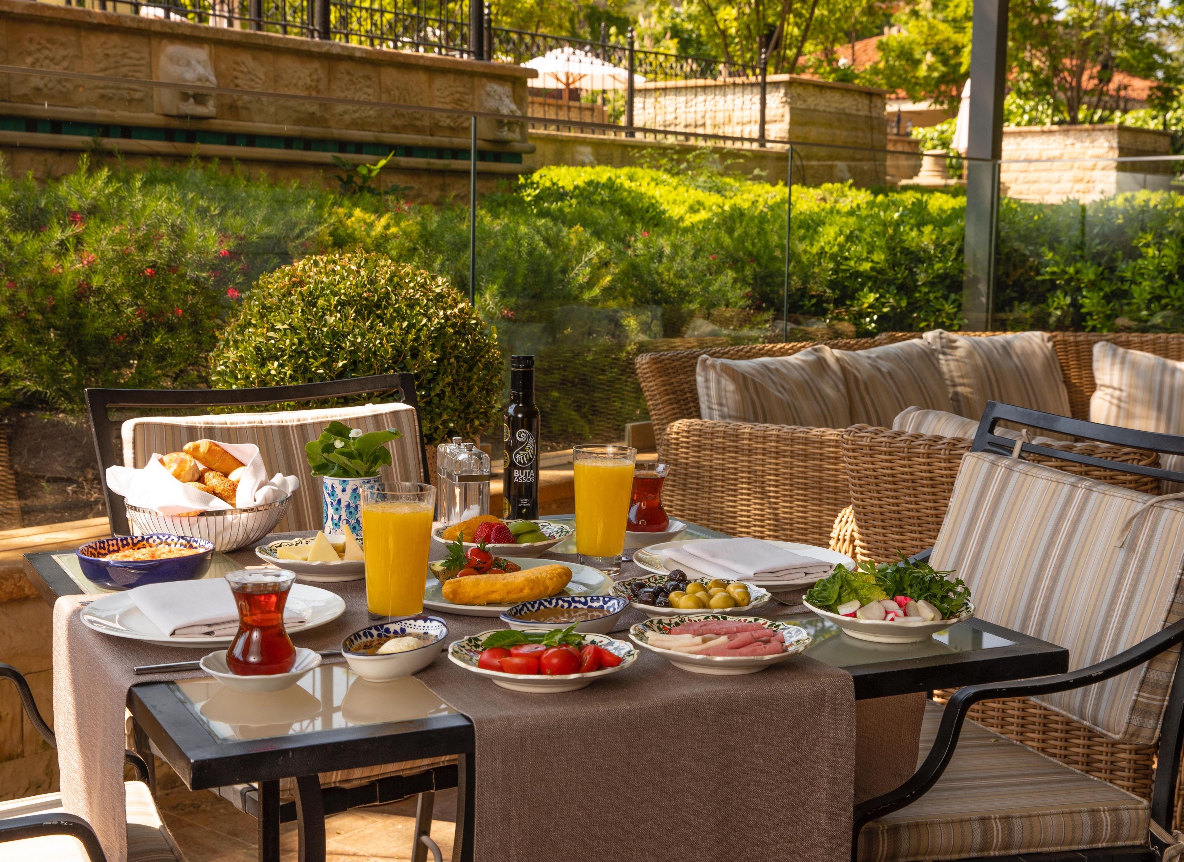 An outdoor dining area with wicker furniture, a table set with plates of food, a bottle, and a glass of orange juice.