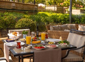 An outdoor dining area with wicker furniture, a table set with plates of food, a bottle, and a glass of orange juice.