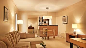 A hotel room with a sofa set, a dining table, a kitchen area, and a lamp.